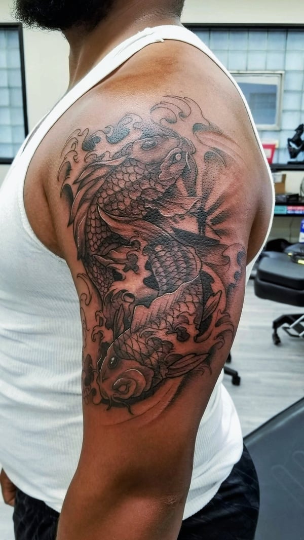 A black and grey Japanese style tattoo of two koi fish surrounded by waves on the upper arm, featuring intricate linework and shading — by Dretty, long beach, ca