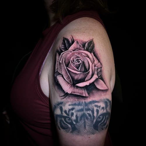 A black and grey realism tattoo on the upper arm featuring a detailed rose with a tiger's eyes below it, showcasing intricate shading and depth — by Travis Ross, los angeles