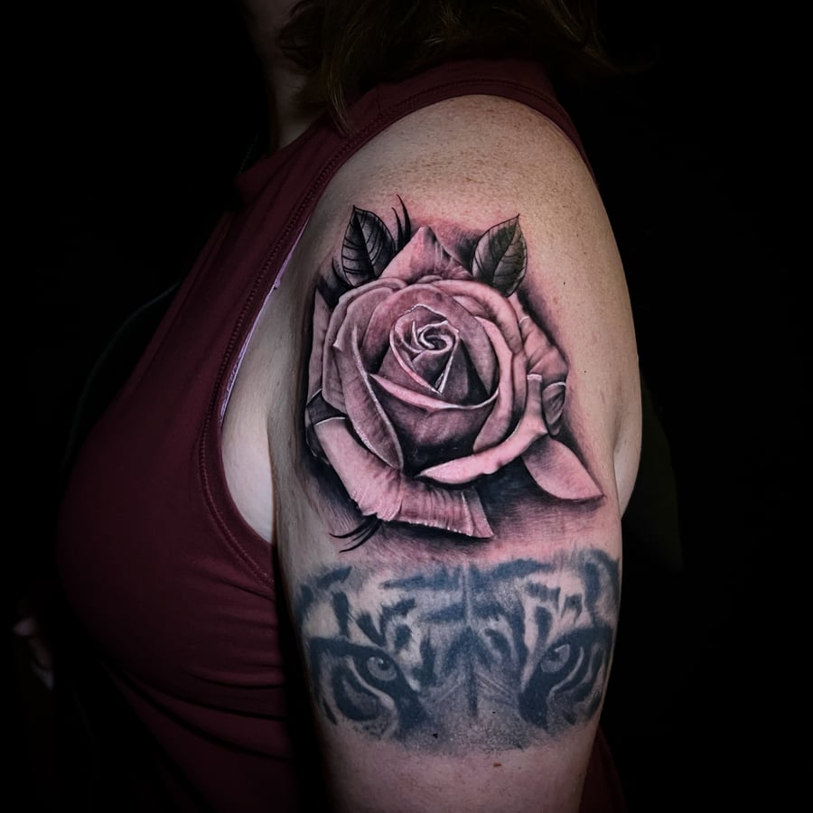 A black and grey realism tattoo on the upper arm featuring a detailed rose with a tiger's eyes below it, showcasing intricate shading and depth — by Travis Ross, los angeles