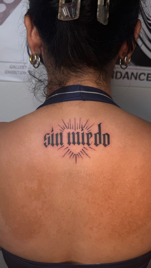 A black and grey lettering tattoo on the upper back with the words 'sin miedo' surrounded by radiating lines — by NJ TATTOOZ, los angeles