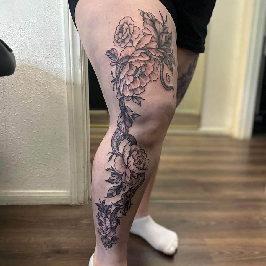 A black and grey fine line tattoo of a snake wrapped in flowers on the leg — by Maddie Ramirez, los angeles