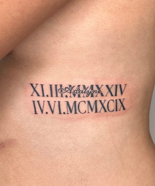A black and grey lettering tattoo on the rib featuring Roman numerals and a name in script style — by NJ TATTOOZ, los angeles