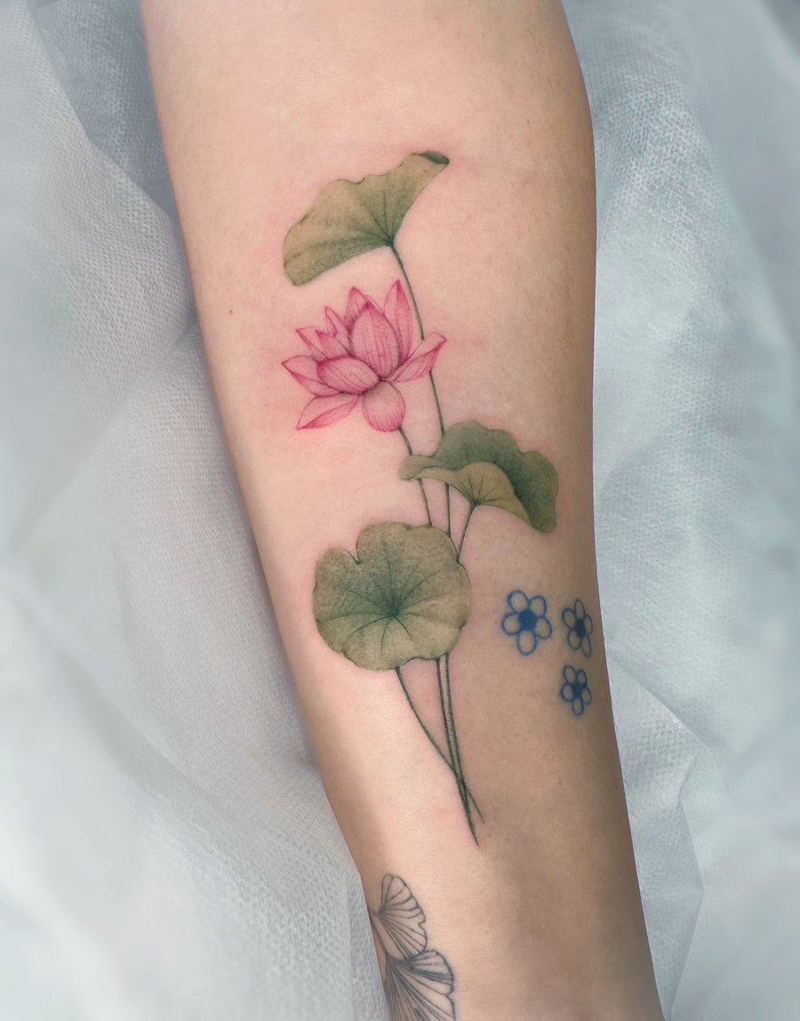 A delicate fine line lotus flower with leaves in color on the forearm, featuring a botanical style — by Melanie Benoit, los angeles