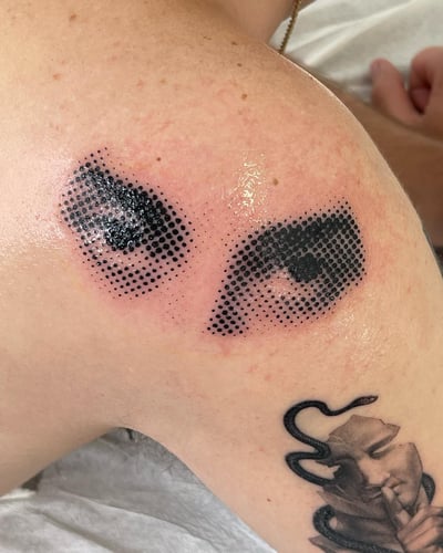 A graphic black and grey dotwork tattoo of eyes on the shoulder, featuring bold dot patterns — by Level tattoo, los angeles