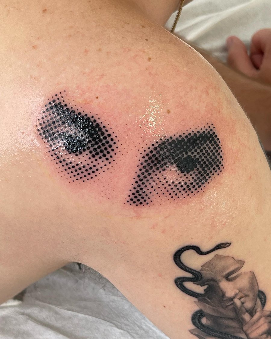 A graphic black and grey dotwork tattoo of eyes on the shoulder, featuring bold dot patterns — by Level tattoo, los angeles