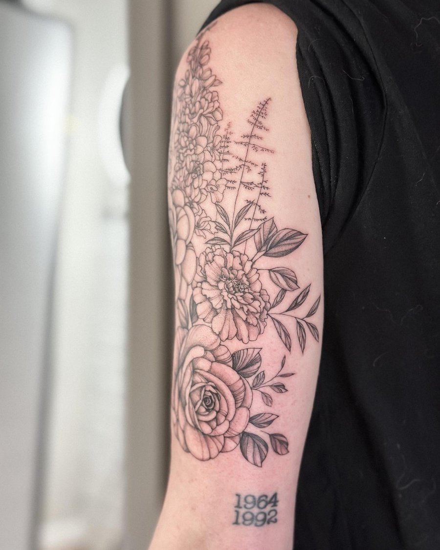 A delicate black and grey floral arrangement tattoo on the upper arm featuring roses and other flowers — by Melanie Benoit, los angeles