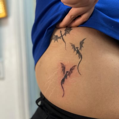 A delicate blackwork tattoo of small dragons on the hip — by Maddie Ramirez, los angeles