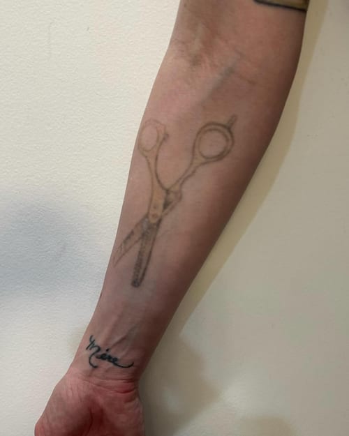 A minimalist black and grey tattoo of scissors on the forearm, featuring a simple and clean design — by Melanie Benoit, los angeles