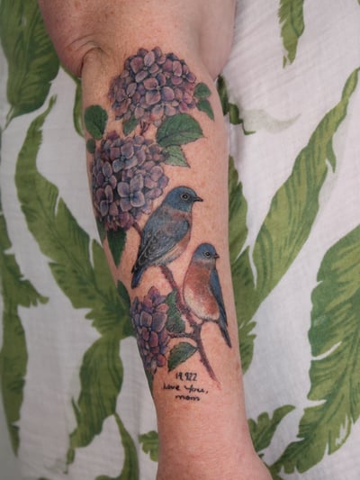A colorful tattoo of birds perched on hydrangeas on the forearm, featuring realistic details and vibrant colors — by Melanie Benoit, los angeles