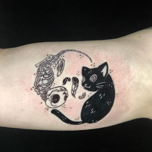 A black and grey yin yang tattoo featuring a cat and a skeleton on the forearm, done in a graphic blackwork style — by Sandra Price, los angeles