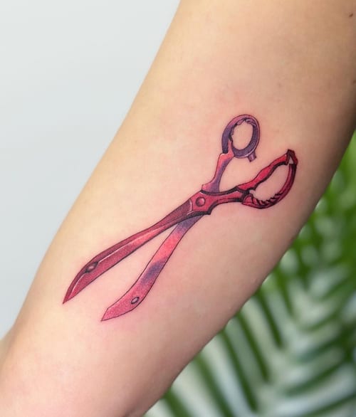 A minimalist tattoo of a pair of scissors on the forearm, featuring fine line work and a subtle use of color — by Jian Liang, los angeles