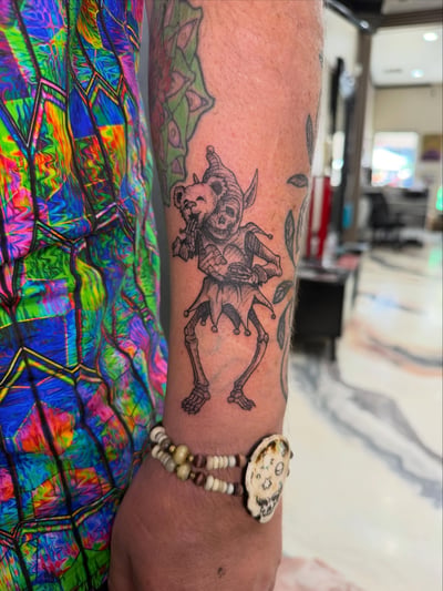 A black and grey skeleton jester tattoo on the forearm with a whimsical and dark style — by Kiera Garvin, los angeles