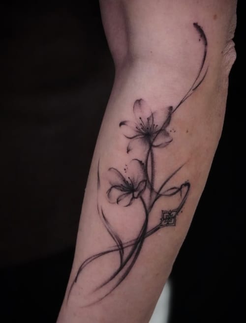 A delicate black and grey fine line floral tattoo on the forearm, featuring two flowers with flowing stems — by Jian Liang, los angeles