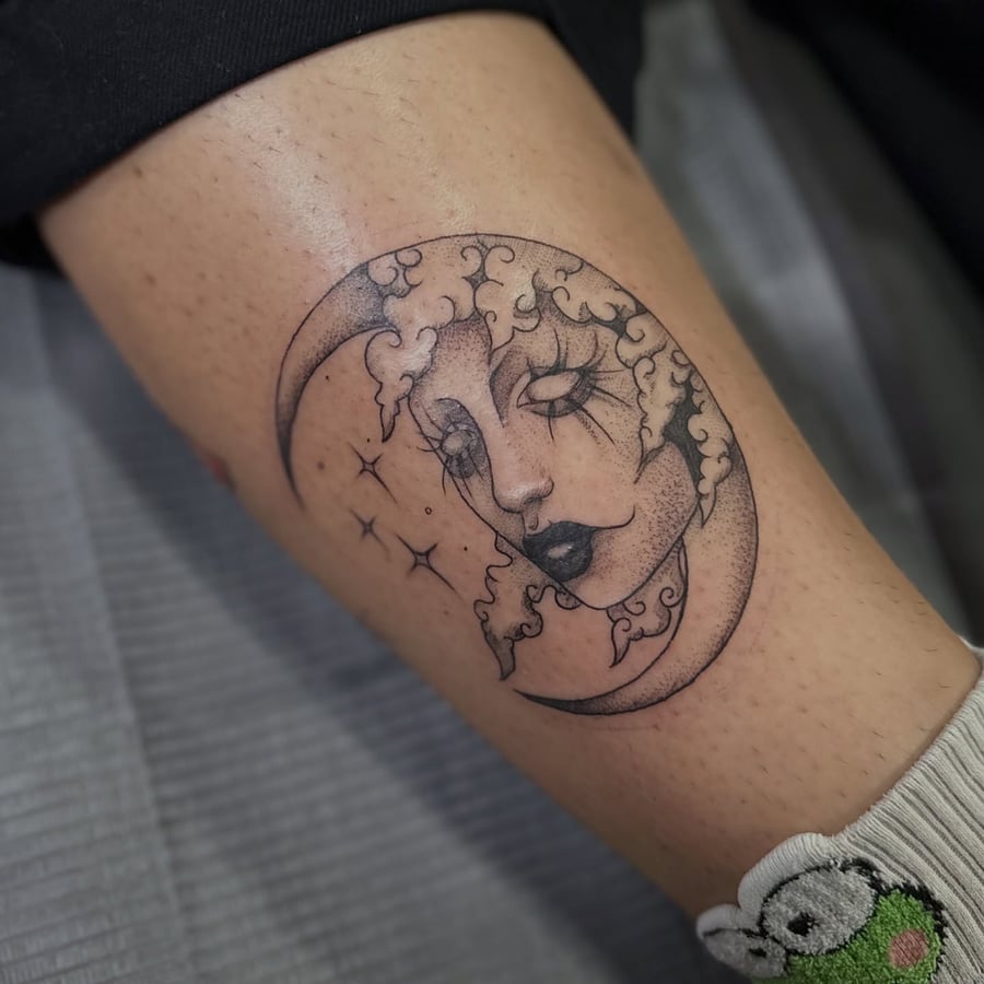 A delicate blackwork tattoo of a moon with a woman's face on the thigh, featuring dotwork shading and surreal elements — by Maddie Ramirez, los angeles