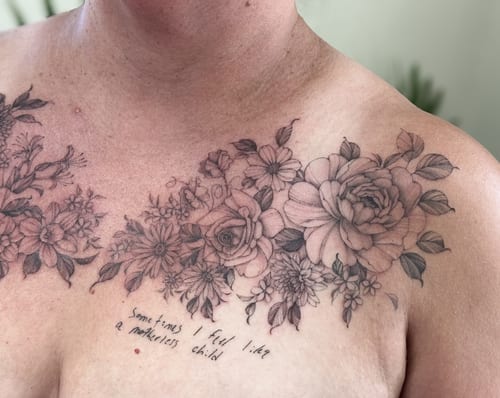 A delicate black and grey floral arrangement with script on the chest, featuring roses and various flowers in fine line style — by Melanie Benoit, los angeles