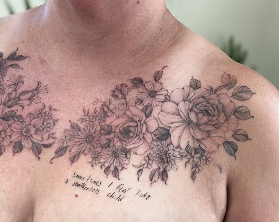 A delicate black and grey floral arrangement with script on the chest, featuring roses and various flowers in fine line style — by Melanie Benoit, los angeles
