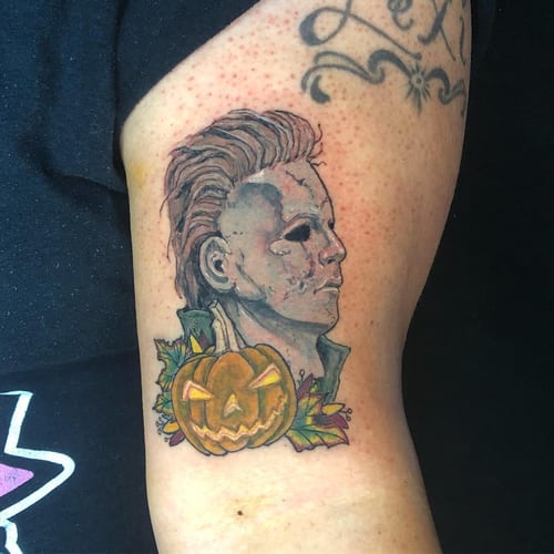 A colorful neo-traditional tattoo of a horror character with a pumpkin on the upper arm, featuring bold lines and graphic details — by Sandra Price, los angeles