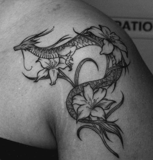 A black and grey tattoo of a dragon intertwined with flowers on the shoulder, featuring bold lines and intricate details — by NJ TATTOOZ, los angeles