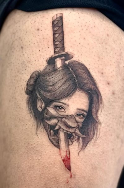 A black and grey illustrative tattoo of a woman's face with a dagger through it, featuring realistic shading and a touch of red ink on the blade, located on the thigh — by otaybeatdown, los angeles