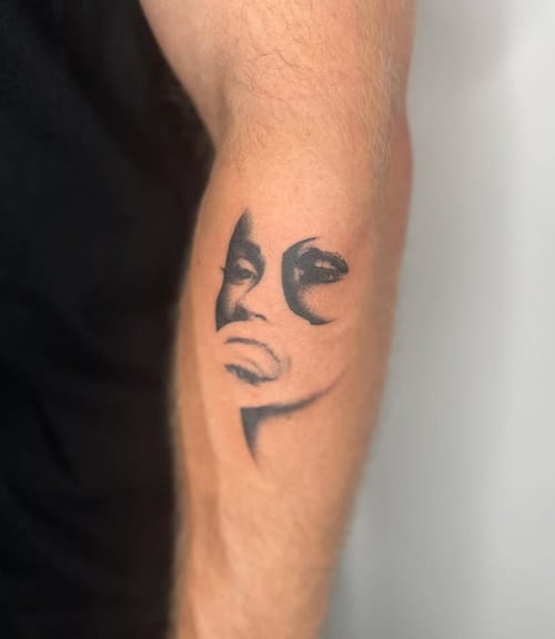 A black and grey portrait tattoo on the forearm, featuring a stylized face with bold shading and abstract elements — by Level tattoo, los angeles