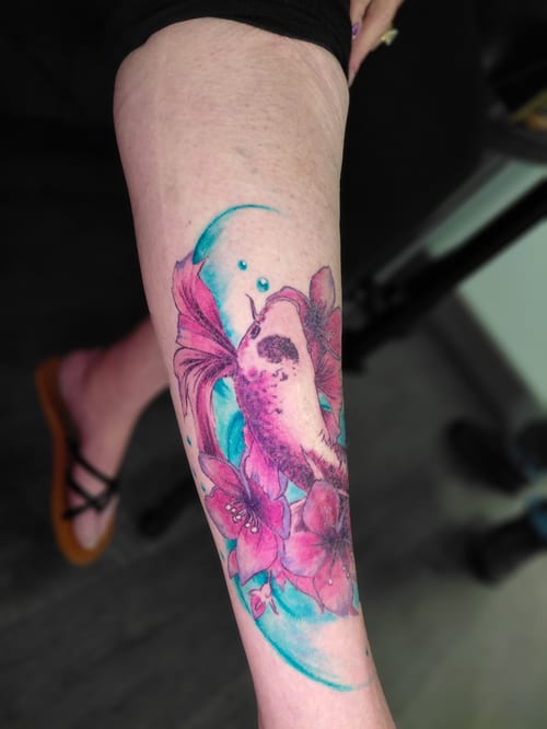A vibrant watercolor tattoo on the calf featuring a koi fish surrounded by pink flowers, with a fluid and artistic style — by anoetic.designs.ultd, los angeles