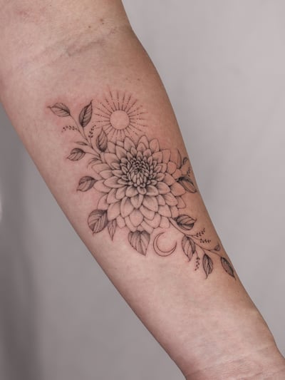A delicate black and grey fine line tattoo of a flower with sun and moon elements on the forearm — by Melanie Benoit, los angeles