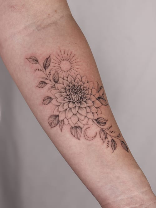 A delicate black and grey fine line tattoo of a flower with sun and moon elements on the forearm — by Melanie Benoit, los angeles