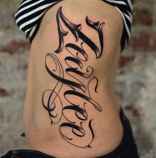 A bold black and grey script lettering tattoo on the rib, featuring elegant and flowing calligraphy — by Johnny Ayala, los angeles