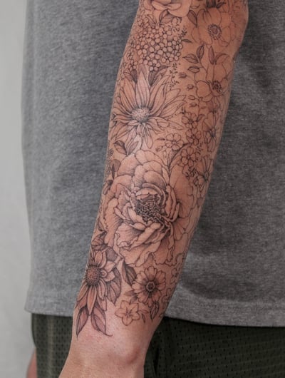 A delicate black and grey floral arrangement tattoo on the forearm featuring various flowers in an ornate design — by Melanie Benoit, los angeles