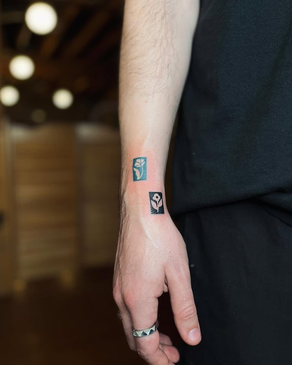 A minimalist blackwork floral design on the forearm, featuring abstract flower shapes in small rectangular frames — by Dylan Aiello, los angeles