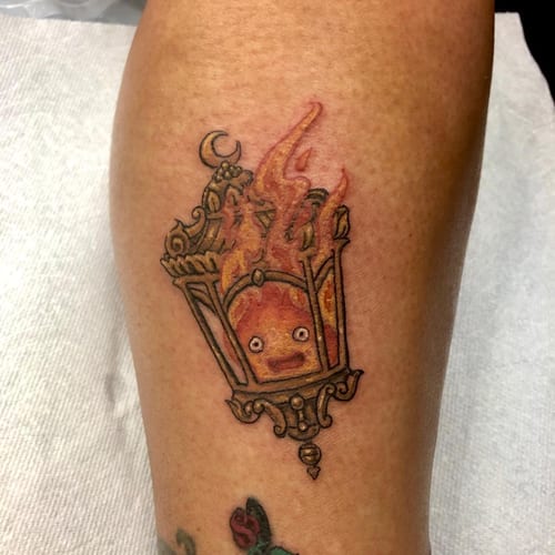 A whimsical and colorful tattoo of a flame character inside a decorative lantern on the leg, featuring an illustrative anime style — by Sandra Price, los angeles