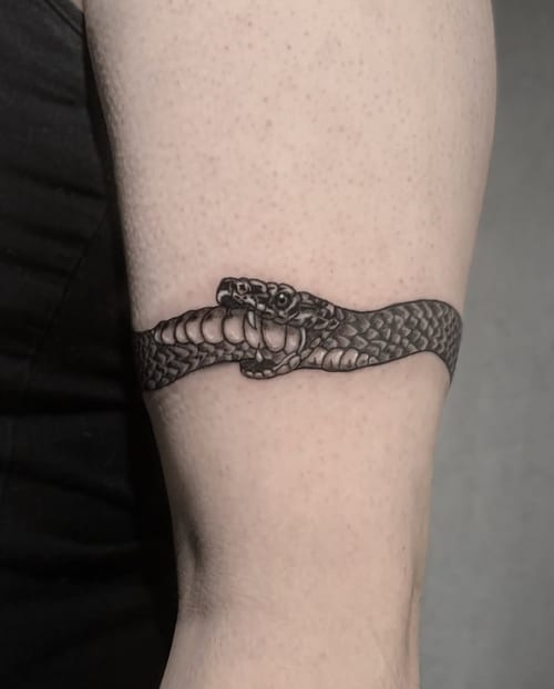 A black and grey linework tattoo of a snake wrapped around the upper arm, featuring detailed scales and a realistic appearance — by Shelby Bianco, los angeles