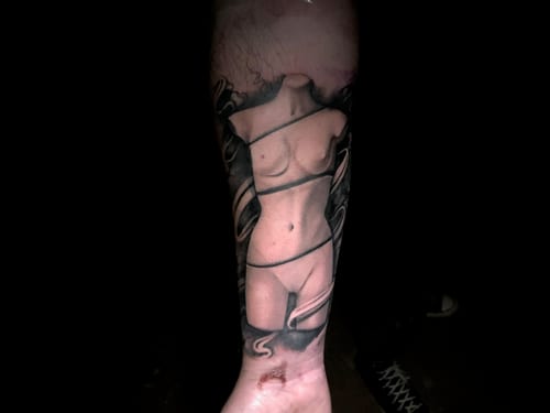 A surreal black and grey tattoo of a headless woman wrapped in ribbons on the forearm, featuring smooth shading and fine detail — by Travis Ross, los angeles