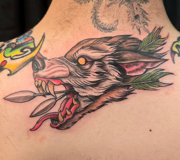 A colorful neo-traditional tattoo of a wolf's head with an arrow through its mouth on the neck, featuring bold lines and vibrant colors — by Dretty, long beach, ca