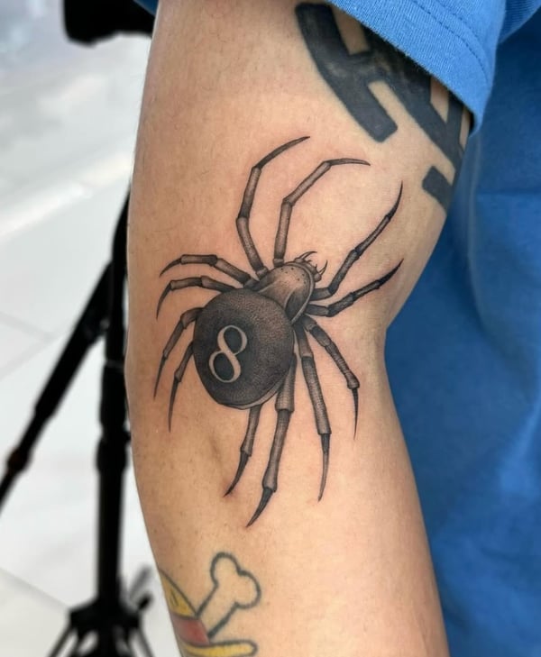 A realistic black and grey tattoo of an eight-legged spider with an '8' on its back, located on the upper arm — by otaybeatdown, orange, ca