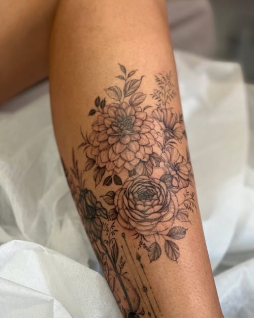 A delicate black and grey floral bouquet tattoo on the leg, featuring detailed flower designs in a blackwork style — by Melanie Benoit, los angeles