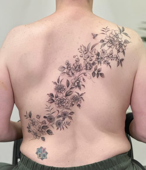 A delicate black and grey floral arrangement tattoo on the back, featuring fine line work and intricate details — by Melanie Benoit, los angeles