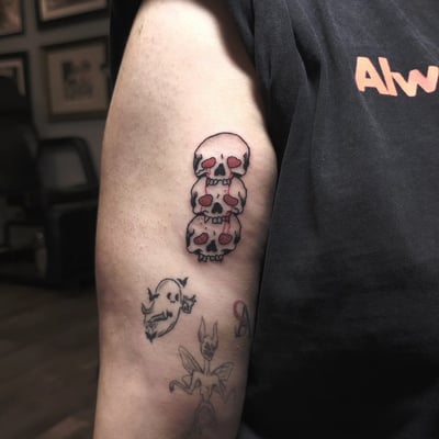 A bold and graphic stack of skulls tattoo on the upper arm, featuring traditional and illustrative styles with red accents — by Miguel ANGELO, los angeles