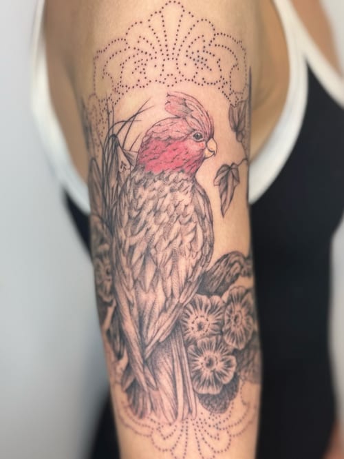 A delicate bird tattoo with flowers on the upper arm, featuring illustrative and dotwork styles with mixed color and black ink — by Samantha Wilks, los angeles
