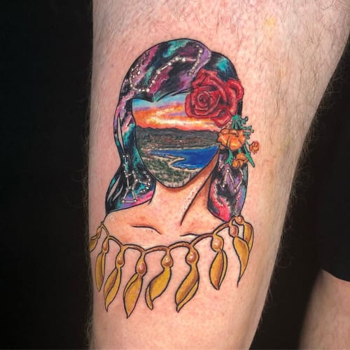 A colorful surreal tattoo of a woman with a landscape as her face, adorned with flowers, on the thigh — by Sandra Price, los angeles