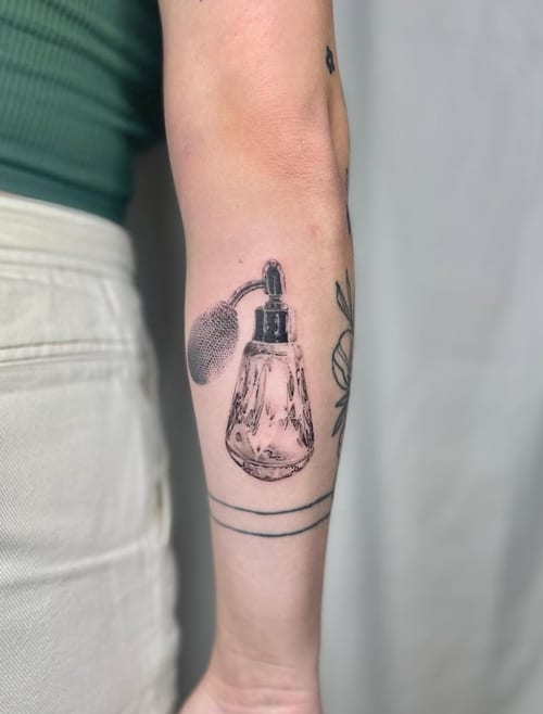 A black and grey realism tattoo of a vintage perfume bottle on the forearm, featuring detailed shading and a classic design — by Level tattoo, los angeles