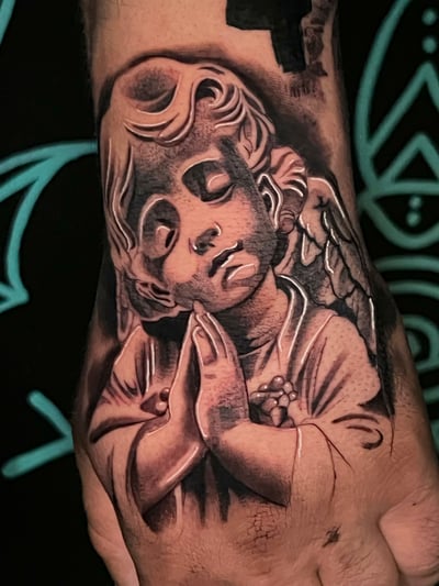A black and grey realistic depiction of an angel with closed eyes and hands in prayer on the hand, featuring detailed shading and highlights — by Josue Bravo, los angeles