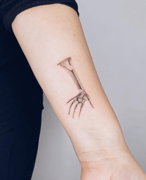 A minimalist fine line tattoo of a skeletal hand and forearm on the forearm, rendered in black and grey — by Level tattoo, los angeles