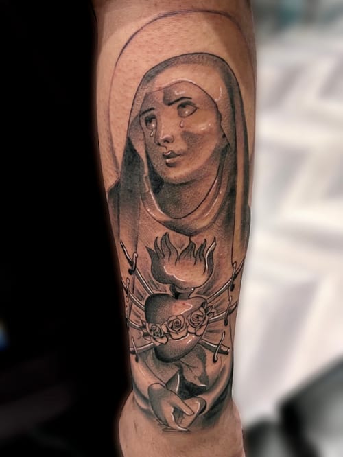 A black and grey realistic depiction of a religious figure on the forearm, featuring a heart with daggers and roses, conveying a solemn and spiritual theme — by Josue Bravo, los angeles