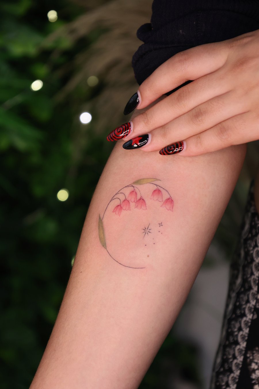 A minimalist color tattoo on the arm featuring a crescent moon with pink flowers and small stars, using fine line work — by gloria.shi.ink, los angeles