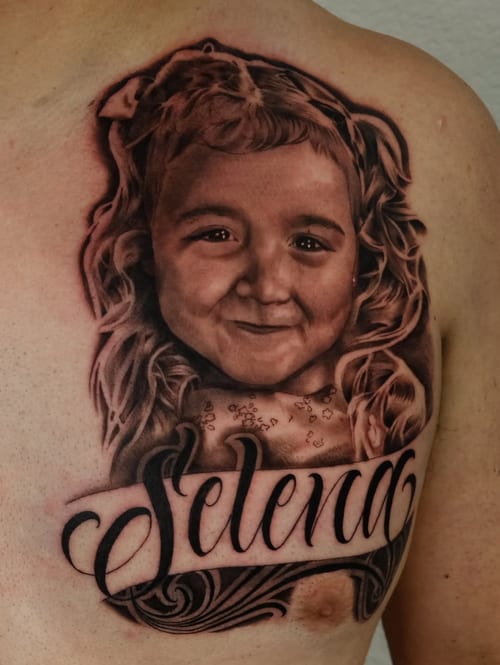 A realistic black and grey portrait of a child with the name 'Selena' on the chest, featuring detailed shading and script lettering — by Johnny Ayala, los angeles