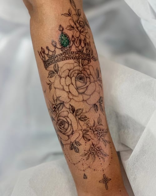 A delicate fine line tattoo of a crown with roses on the leg, featuring blackwork and subtle color accents — by Melanie Benoit, los angeles