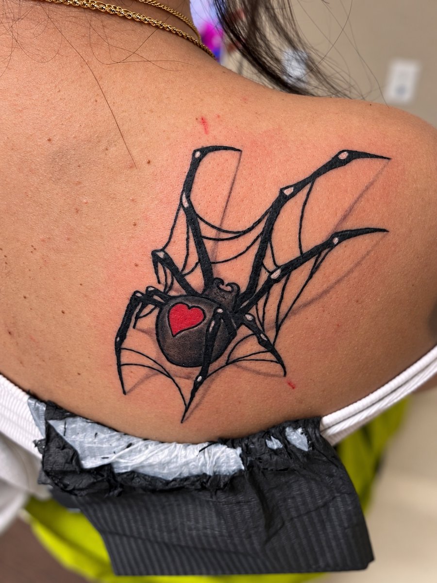 A bold blackwork spider tattoo on the shoulder with a red heart on its back, featuring graphic and illustrative elements — by HEAVY INK, los angeles