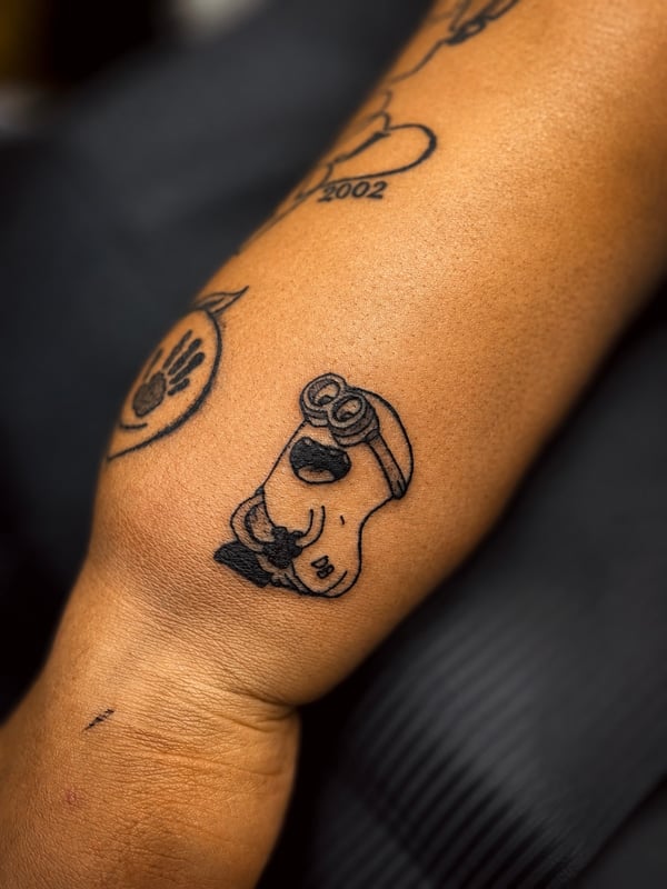 A whimsical blackwork cartoon character tattoo on the forearm, featuring minimalist linework — by HEAVY INK, chino, ca