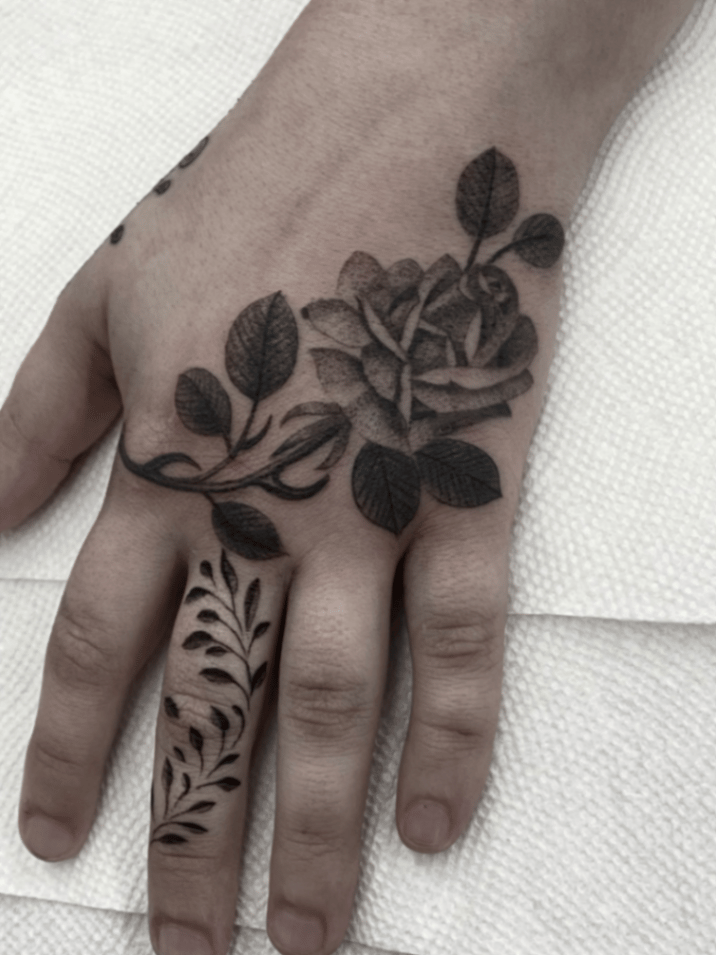 A black and grey floral tattoo on the hand featuring a rose and leaves with intricate detailing — by tyler_whitlock, los angeles